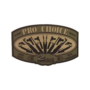 Puede incluir: Una pegatina ovalada de color marrón claro y marrón con el texto "Pro-Choice" y "2nd Amendment" en una fuente estilizada. La pegatina presenta una variedad de armas de fuego en forma de abanico con el texto "Any Gun Any Where" en la parte inferior.