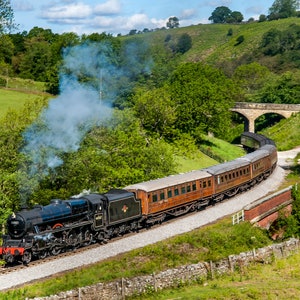 May include: A black steam locomotive pulls a train of brown passenger cars along a curved track through a green valley. The train is emitting smoke and steam.