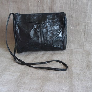Può includere: Borsa a tracolla in pelle nera con una tracolla lunga e sottile. La borsa presenta un design patchwork con cuciture geometriche e un piccolo accento ovale sul davanti. La borsa è di piccole dimensioni.