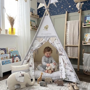 May include: A child's play tent with a lion emblem and the name "Franklin" is set up in a nursery. The tent is surrounded by animal-themed toys, books, and decorative pillows. The room has a starry wallpaper and a neutral color scheme.