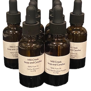 May include: Several amber glass bottles with black droppers are arranged in a group. Each bottle has a white label with text that reads "Mill Creek Soap and Candles" and the scent name. The bottles contain 1 oz (27g) of oil.