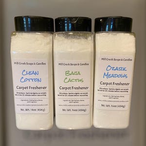 May include: Three clear plastic containers of carpet freshener with black lids. Each label reads "Clean Cotton," "Baja Cactus," and "Ozark Meadows." The labels also include directions, ingredients, and the product's net weight of 16 oz (454g).