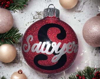 Könnte beinhalten: Roter Glitzer-Weihnachtsbaumschmuck mit dem Namen "Sawyer" in silbernem Glitzer auf schwarzem Hintergrund.