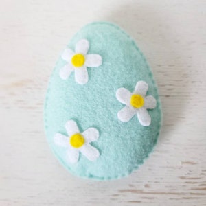 May include: A light blue felt Easter egg with three white felt flowers with yellow centers.