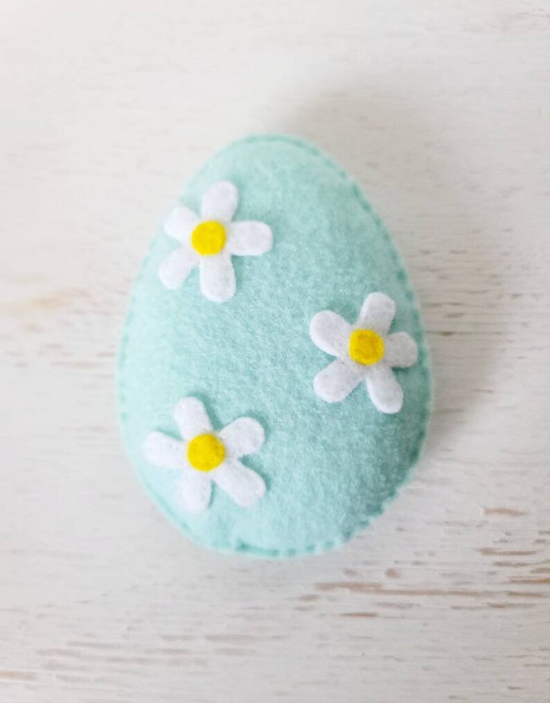 May include: A light blue felt Easter egg with three white felt flowers with yellow centers.