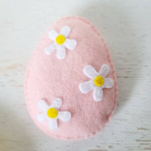May include: A pink felt Easter egg with three white felt flowers with yellow centers.