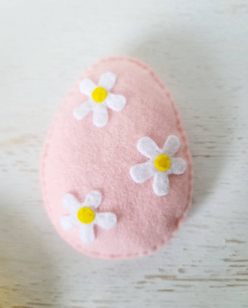 May include: A pink felt Easter egg with three white felt flowers with yellow centers.