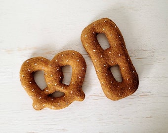 Pode incluir: Dois alimentos de feltro: um pretzel castanho e um pau de pretzel castanho. Ambos são decorados com costuras brancas.