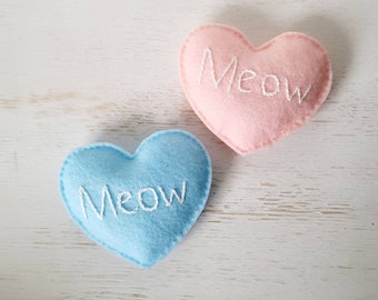 May include: Two felt heart-shaped pillows, one light blue and one light pink, with the word "Meow" embroidered in white on each.
