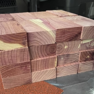 May include: A stack of cedar wood blocks, each block is approximately 2 inches wide and 4 inches long. The blocks are a deep reddish-purple color with a natural wood grain pattern.