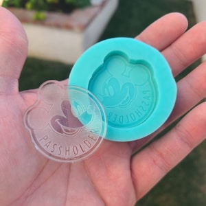 May include: A clear plastic keychain with a Mickey Mouse design and the text "PASSHOLDER" around the edge. The keychain is next to a blue silicone mold with the same Mickey Mouse design.