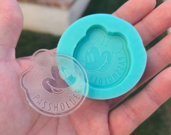 May include: A clear plastic keychain with a Mickey Mouse design and the text "PASSHOLDER" around the edge. The keychain is next to a blue silicone mold with the same Mickey Mouse design.
