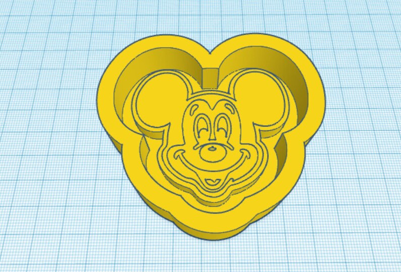 May include: Yellow plastic cookie cutter shaped like Mickey Mouse's head. The cutter has a detailed outline of Mickey Mouse's face, including his ears, eyes, nose, and smile.