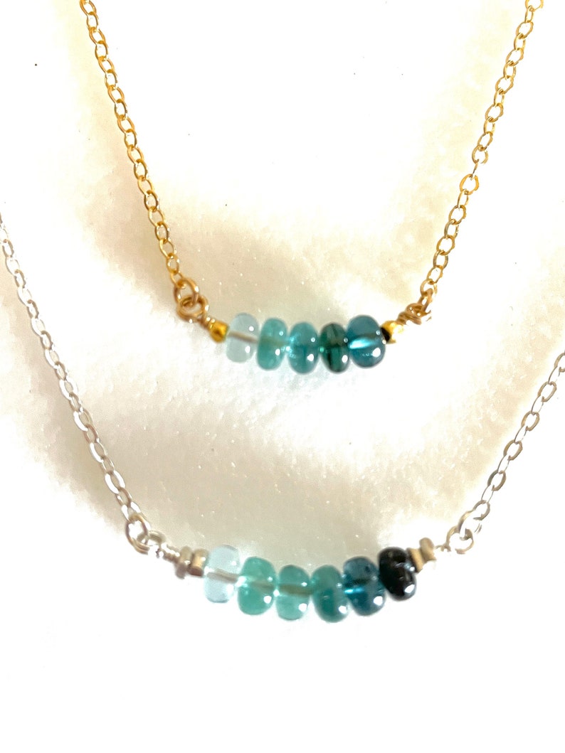 May include: Two delicate necklaces with graduated blue gemstone beads. The top necklace has a gold chain and the bottom necklace has a silver chain.