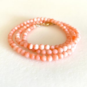 May include: A delicate necklace made of pink coral beads. The necklace is layered and features a gold clasp.