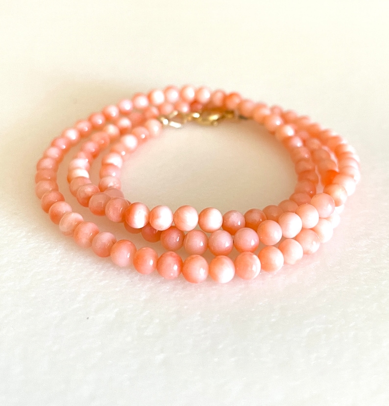 May include: A delicate necklace made of pink coral beads. The necklace is layered and features a gold clasp.
