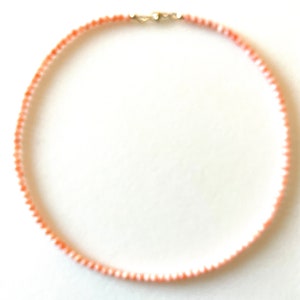 May include: A delicate necklace made of small, pink and white coral beads. The necklace is strung on a silver chain and has a silver clasp.