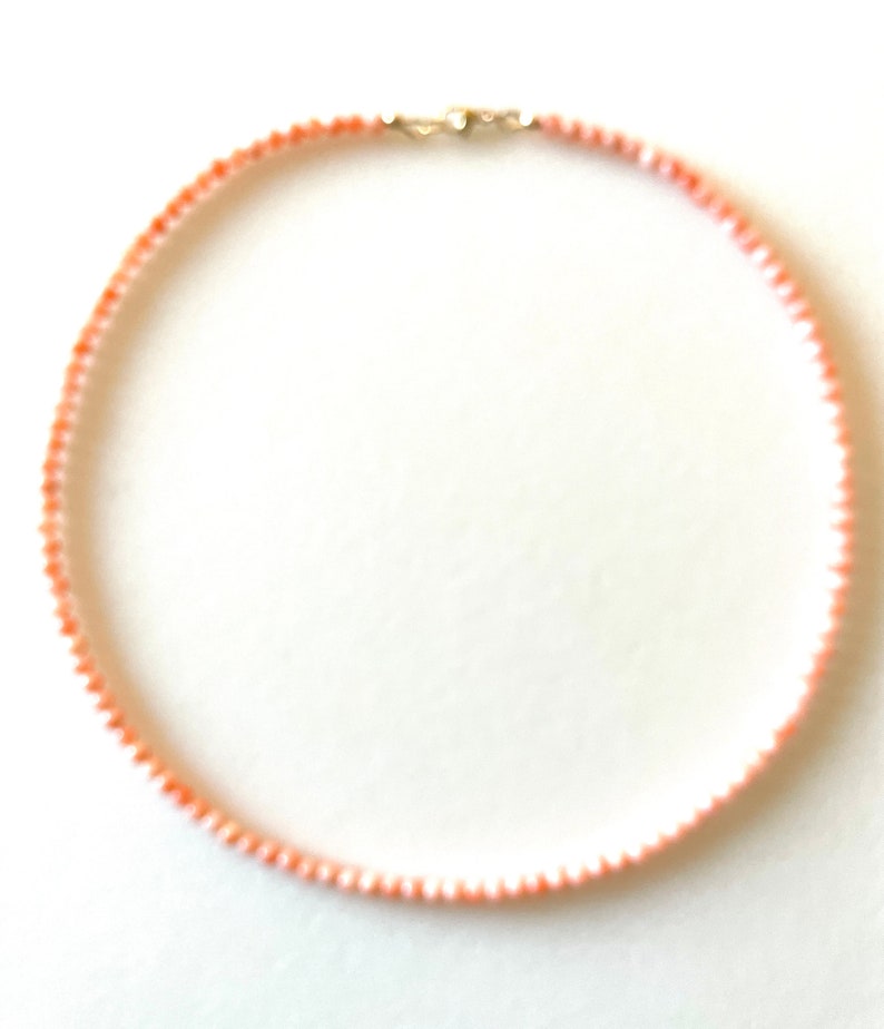 May include: A delicate necklace made of small, pink and white coral beads. The necklace is strung on a silver chain and has a silver clasp.