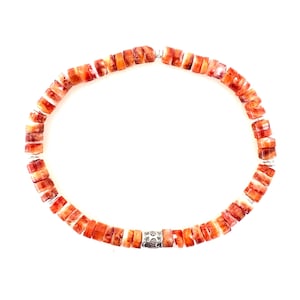 May include: A beaded bracelet featuring rectangular orange and white beads. The bracelet has a silver-colored clasp with a floral design. The beads are strung together with a silver-colored wire.