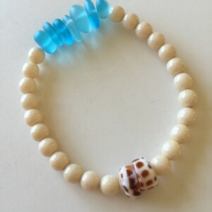 May include: A white bead bracelet with a brown and white seashell charm and blue glass beads.