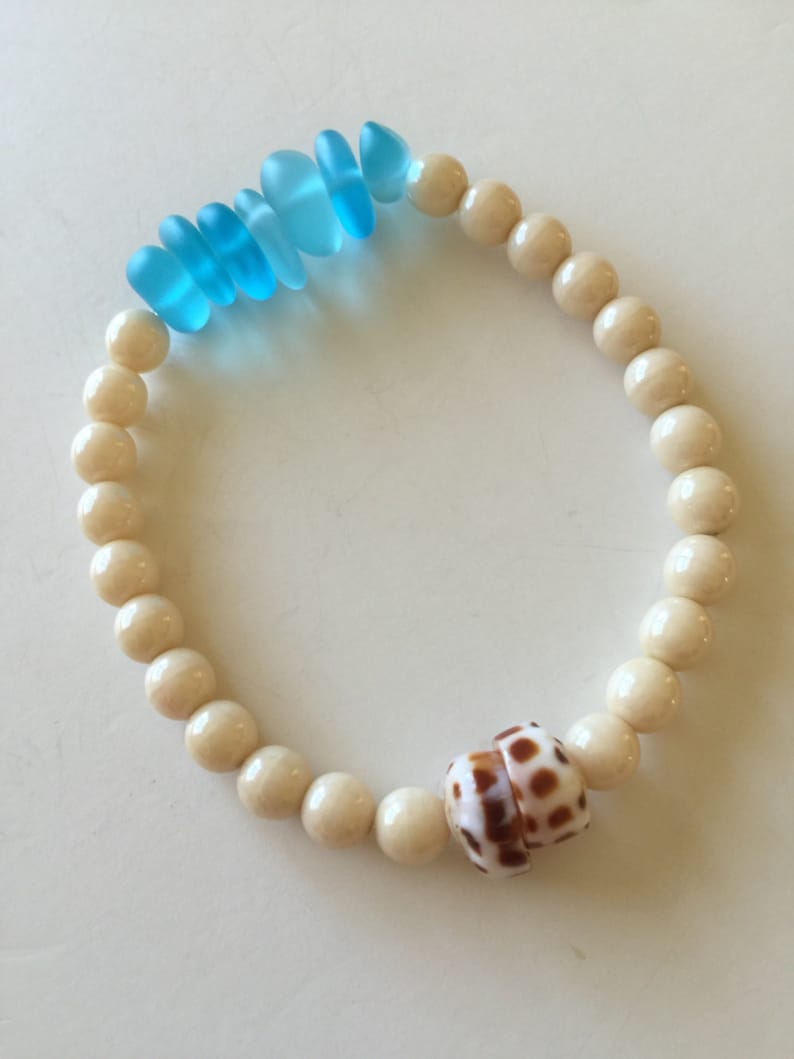 May include: A white bead bracelet with a brown and white seashell charm and blue glass beads.