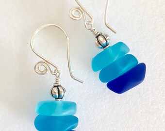 Könnte beinhalten: Ein Paar silberne Ohrhänger mit drei Schichten blauen Meerglass. Das Meerglass ist von hellblau bis dunkelblau geschichtet. Die Ohrringe haben oben eine silberne Perle.
