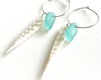 May include: A pair of silver hoop earrings with a white seashell and a light blue sea glass charm hanging from each hoop.