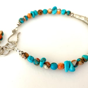 May include: A turquoise, brown, and orange beaded bracelet with a silver clasp and a silver fishtail charm.