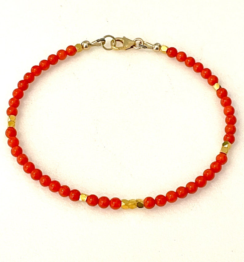 Pode incluir: Uma pulseira delicada com pequenas contas redondas laranja. O design incorpora contas douradas de forma geom&eacute;trica. A pulseira &eacute; fechada com um fecho dourado. As contas t&ecirc;m cerca de 0,3 cm de di&acirc;metro.