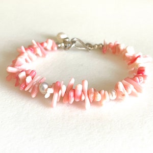 Könnte beinhalten: Ein pinkfarbenes und weißes Korallenarmband mit einem silbernen Verschluss und Perlenakzenten.
