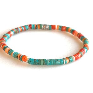 May include: A colorful beaded bracelet featuring turquoise, orange, red, and white beads. The bracelet is strung on a flexible cord and has a silver-colored clasp. The beads are small and round, creating a vibrant accessory.