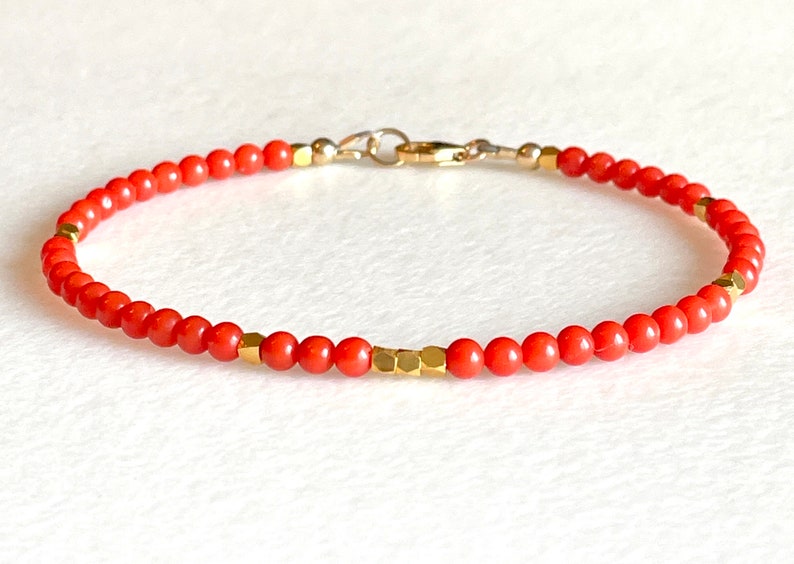 Pode incluir: Uma pulseira delicada com pequenas contas redondas de cor coral. Contas geom&eacute;tricas douradas e um fecho dourado adicionam contraste. A pulseira foi projetada para uma est&eacute;tica minimalista.