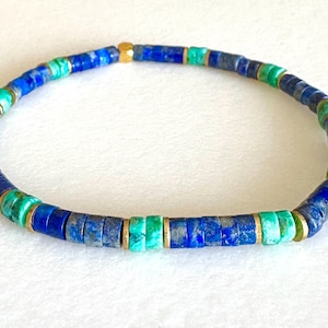 Può includere: Un braccialetto di perline composto da piccole perline piatte e circolari blu e verdi, intervallate da elementi dorati. Il design flessibile presenta un mix di pietre blu e turchese. L'insieme è impreziosito da accenti dorati.