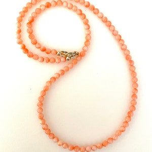 May include: A delicate coral necklace with a gold clasp. The necklace is made of small, round coral beads.