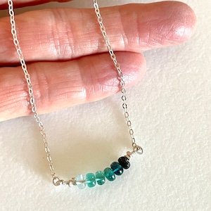 May include: A silver chain necklace with a graduated row of light blue to dark blue gemstones.