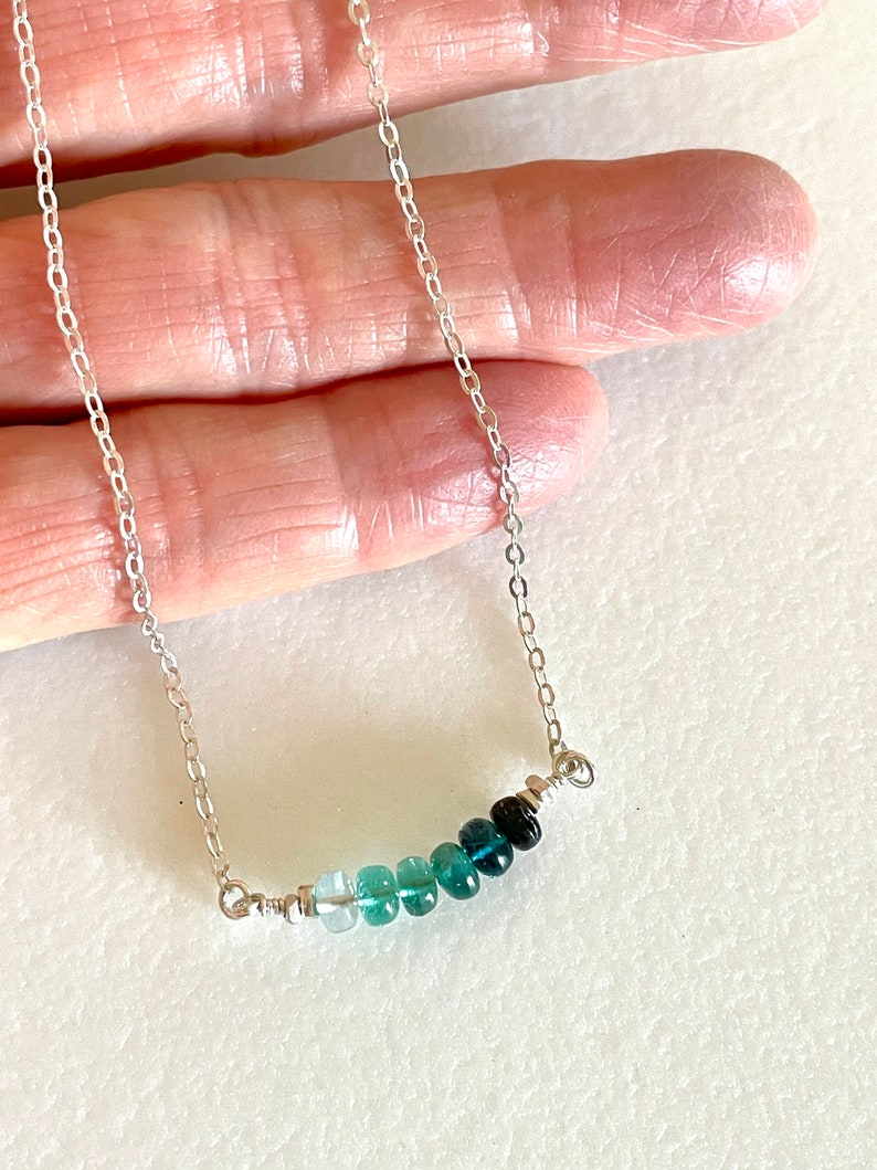 May include: A silver chain necklace with a graduated row of light blue to dark blue gemstones.