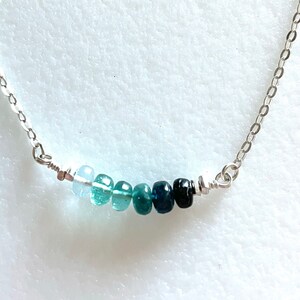 May include: A silver chain necklace with a graduated row of blue gemstones. The stones range in colour from light blue to dark blue.