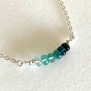 May include: A silver chain necklace with a graduated row of blue gemstone beads. The beads range in colour from light blue to dark blue.