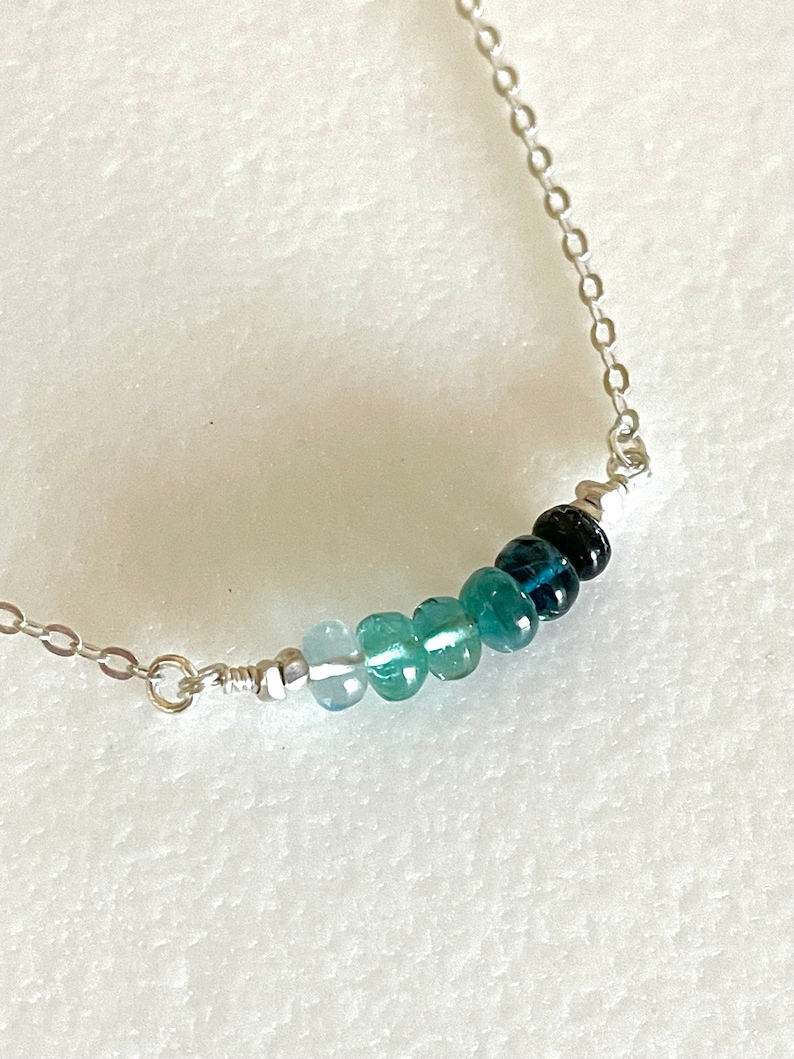 May include: A silver chain necklace with a graduated row of blue gemstone beads. The beads range in colour from light blue to dark blue.