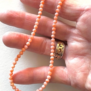 May include: A delicate necklace made of small, round, light pink coral beads. The necklace is strung on a thin cord and is approximately 18 inches long.