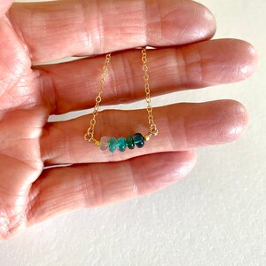 May include: A gold chain necklace with a row of graduated green gemstones. The necklace is delicate and features a subtle ombre effect.