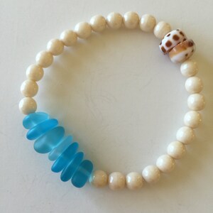 May include: A white bead bracelet with a blue glass bead accent and a shell charm.