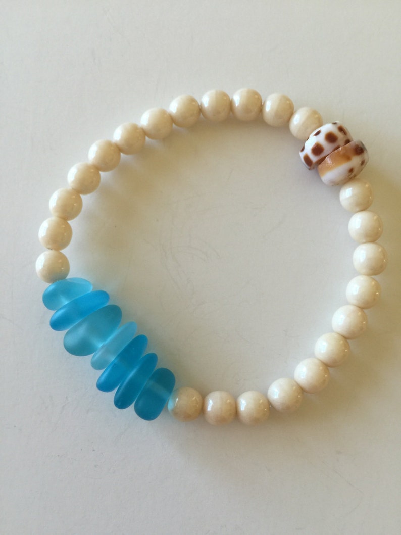 May include: A white bead bracelet with a blue glass bead accent and a shell charm.