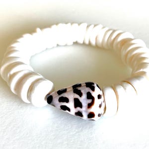 May include: White shell bracelet with a brown and white seashell charm.