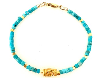 May include: A turquoise and gold beaded bracelet with a gold charm. The charm has a detailed design.