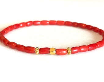May include: A red coral beaded bracelet with gold accents. The bracelet has a single larger gold bead in the centre.