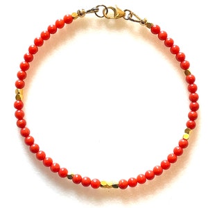 Pode incluir: Uma pulseira delicada com pequenas contas redondas de cor coral enfiadas juntas. A pulseira &eacute; adornada com contas douradas de formato geom&eacute;trico e um fecho dourado. O design &eacute; simples e elegante, adequado para uso di&aacute;rio.