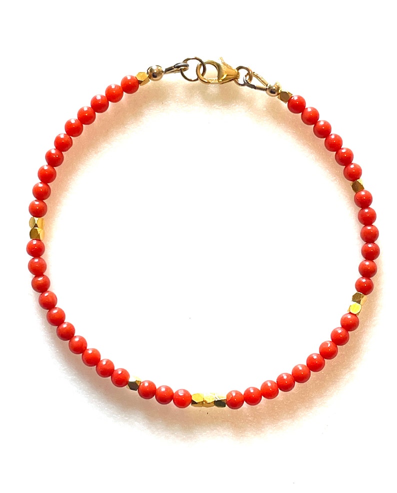 Pode incluir: Uma pulseira delicada com pequenas contas redondas de cor coral enfiadas juntas. A pulseira &eacute; adornada com contas douradas de formato geom&eacute;trico e um fecho dourado. O design &eacute; simples e elegante, adequado para uso di&aacute;rio.