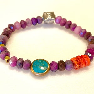 May include: A purple gemstone bracelet with a turquoise stone and coral accents. The bracelet has a silver clasp and gold beads.