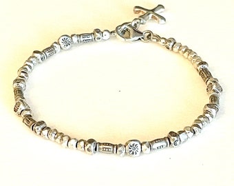 May include: A silver bracelet with a cross charm and small silver beads. The beads have different designs, including a flower and a geometric pattern.